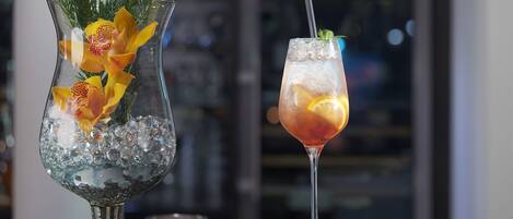 Dos bebidas sobre una barra, una en una jarra de vidrio y otra en una copa de martini, con hielo y adornos.