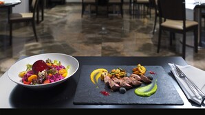 A dining table with a plate of colorful salad and sliced meat, set in a restaurant with multiple tables and chairs.