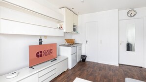Ein modernes Hotelzimmer mit Flachbildfernseher, einem 'GUEST READY' Schild, einer Mikrowelle, einem kleinen Waschbecken, einem Mülleimer und einer Tür mit Spiegel.