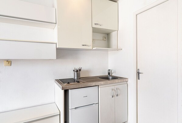 A compact kitchenette with a built-in stove, sink, and a small refrigerator. - GuestReady - Parisian Life near Bastille Plaza (Paris)