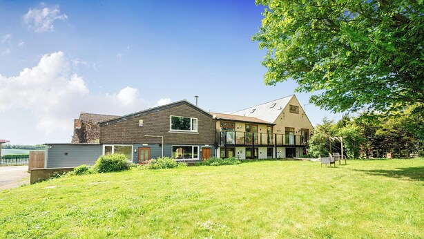 A two-story house with a large lawn, a visible garage, and a tree to the right. - Relaxing Room With Ensuite Rutland Point (Oakham)