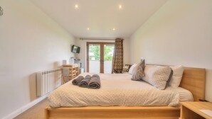 A bedroom with a wooden bed, a desk, a chair, a radiator, and a TV on the wall. - Relaxing Room With Ensuite Rutland Point (Oakham)
