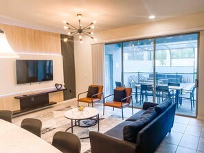 Uma sala de estar moderna com televisão, sofá, cadeiras e um espaço de jantar.