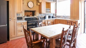 A kitchen with wooden cabinets, a stove, a dining table with chairs, and a clock on the wall. - The Cottage (Belper)