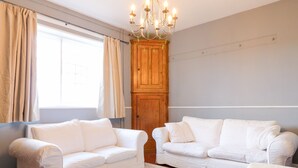 A room with two white sofas, a wooden cabinet, and a chandelier. - The Cottage (Belper)