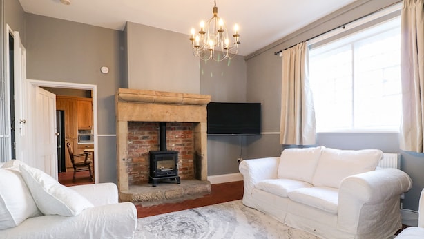 A living room with a fireplace, white sofas, a chandelier, and a flat-screen TV. - The Cottage (Belper)