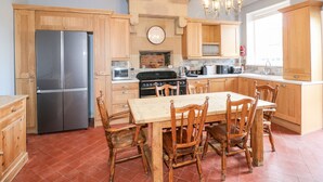 A kitchen with wooden cabinets, a stainless steel refrigerator, a stove, and a dining table with chairs. - The Cottage (Belper)