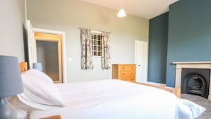 A neatly arranged bedroom with a bed, a dresser, a lamp, and a fireplace. - The Cottage (Belper)
