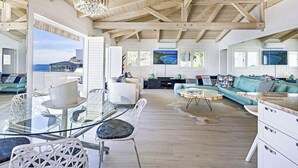Amplia sala de estar con techo alto, mesa de vidrio para comer y vista a la playa.