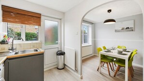 A modern kitchen with a built-in oven, a sink, and a window with blinds. There is a dining area with a table and chairs.