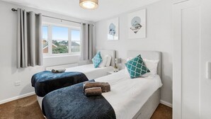 A hotel room with two beds, a window with curtains, a ceiling light, and artwork on the wall.