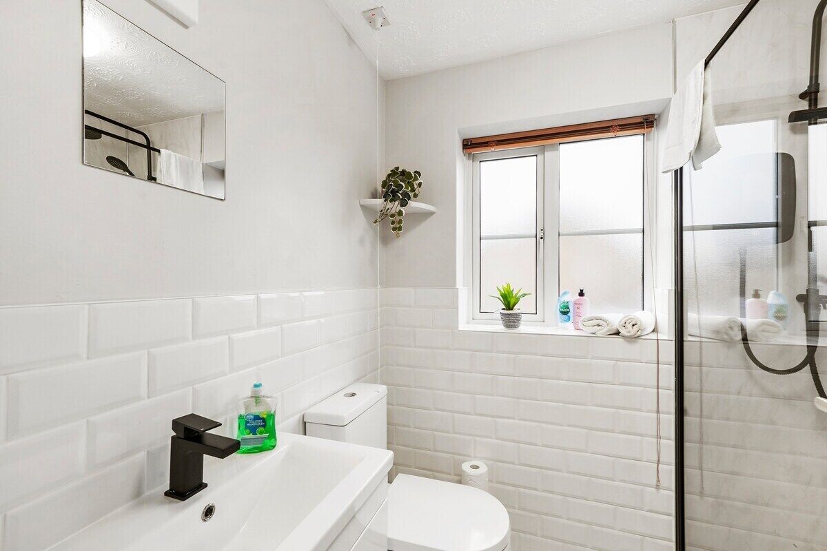 A modern bathroom with white subway tiles, a white sink, a black faucet, a toilet, and a glass shower enclosure.