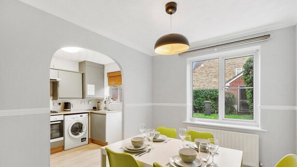 A compact kitchen with a washing machine, a dining area with a table set for four, and a window with a view of a garden.