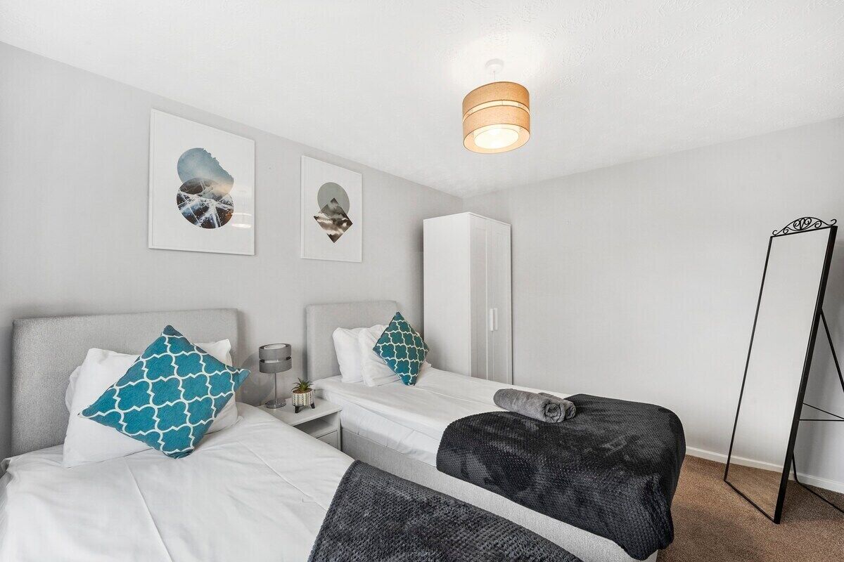Una habitación de hotel moderna con dos camas individuales, un armario, un espejo y obras de arte en la pared.