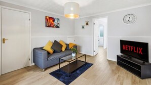 A living room with a grey sofa, a coffee table, a TV, and a wall clock.