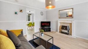 A living room with a sofa, a coffee table, a fireplace, a television, and a hanging light fixture.