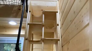 A wooden ladder shelf unit against a paneled wall, with a window and a visible green hose in the background. - Yeti's Tree House: Where Magic Happens (Portland)