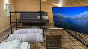 A wooden cabin room with a bed, a couch, and a television displaying a scenic view. - Yeti's Tree House: Where Magic Happens (Portland)