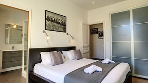 A modern bedroom with a large bed, a dark headboard, and a grey accent wall.