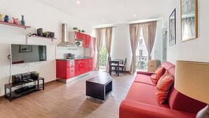 Un salon moderne avec un canapé rouge, un téléviseur, une cuisine aux meubles rouges et un balcon avec une table et des chaises.