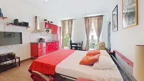 Une chambre d’hôtel équipée d’un lit, d’une télévision, d’une kitchenette et d’un balcon avec des rideaux.