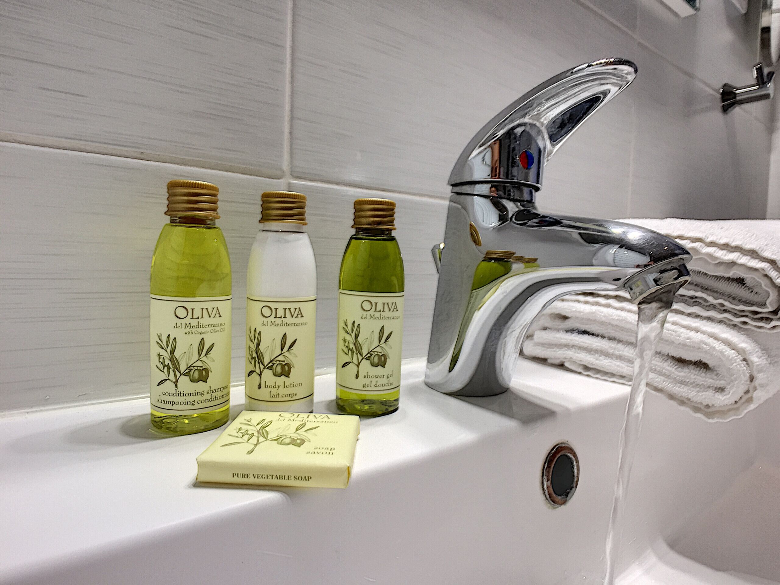 Un baño con un lavamanos blanco, tres botellas de aceite de oliva y una pastilla de jabón.