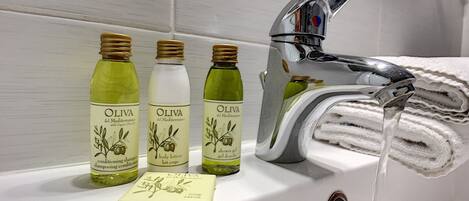 Un baño con un lavamanos blanco, tres botellas de aceite de oliva y una pastilla de jabón.