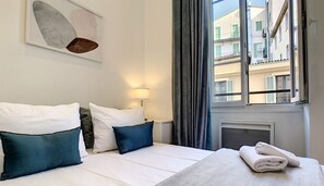 Quarto de hotel com duas camas, uma janela com cortinas, um radiador e uma toalha sobre a cama.