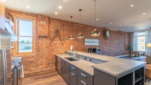 Une cuisine moderne avec un mur en briques, des appareils électroménagers en acier inoxydable et des luminaires suspendus.