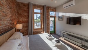 Une chambre d’hôtel moderne avec un mur en briques, un grand lit, un téléviseur à écran plat et un balcon avec vue.