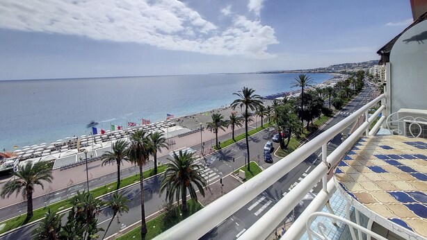 A balcony with a view of a beach, palm trees, and a road with cars.