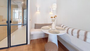 A modern living room with a white sofa, a round table with a vase of flowers, and a glass door leading to another room.