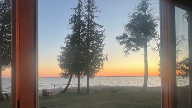 A view from a window overlooking a grassy area with trees and a body of water during sunset. - The Upper Peninsula's Hidden Gem (Rapid River)
