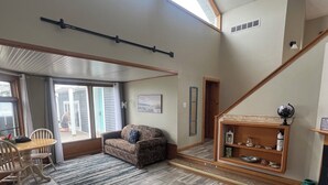 A spacious living area with a high ceiling, a dining table with chairs, a blue sofa, and a staircase leading to an upper level. - The Upper Peninsula's Hidden Gem (Rapid River)