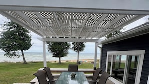 A covered outdoor patio with a table and chairs, overlooking a beach. - The Upper Peninsula's Hidden Gem (Rapid River)