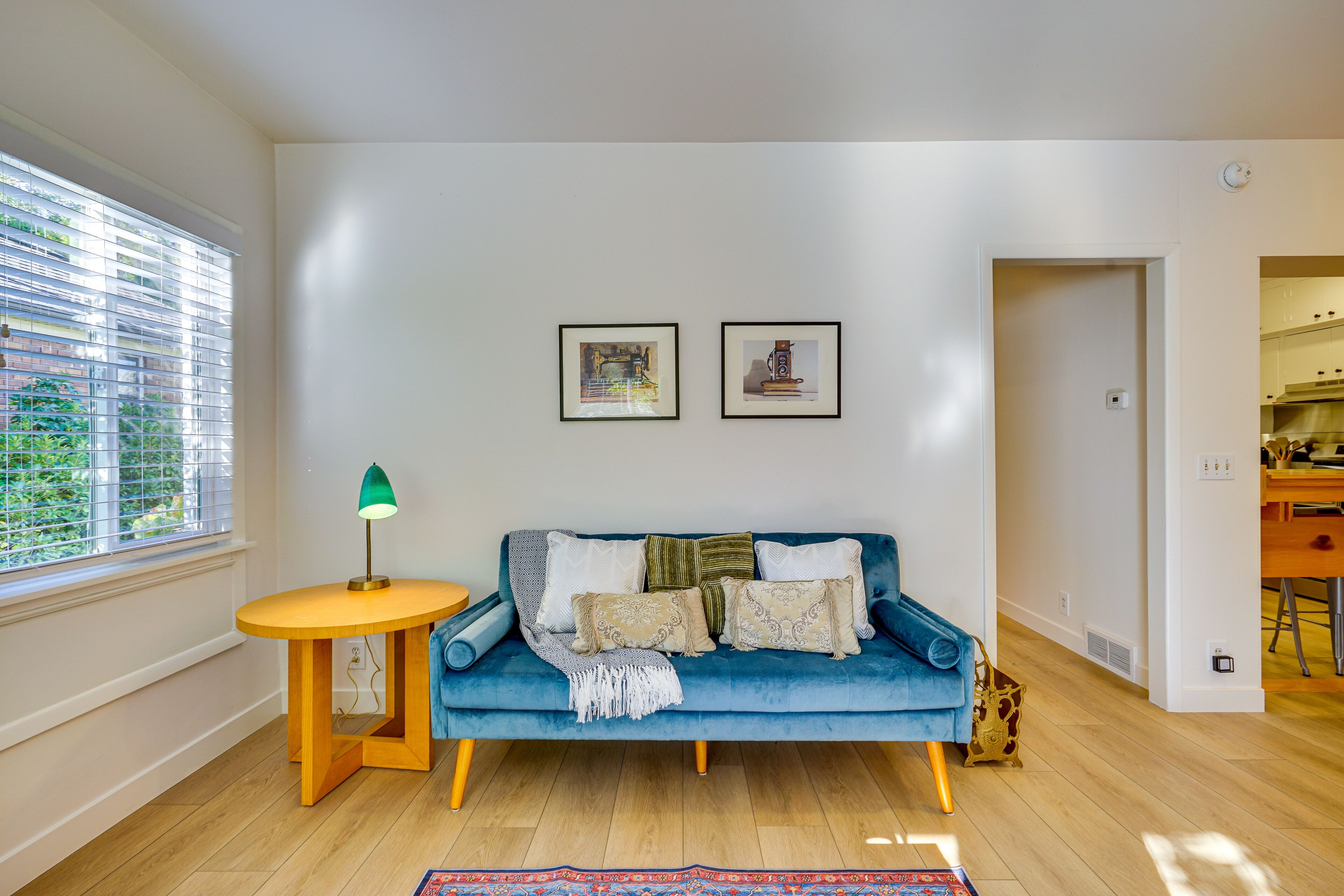 A living room with a blue sofa, a small round table with a lamp, and two framed pictures on the wall.