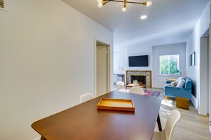 Een moderne woonkamer met een open haard, een blauwe bank en een eethoek met een houten tafel.