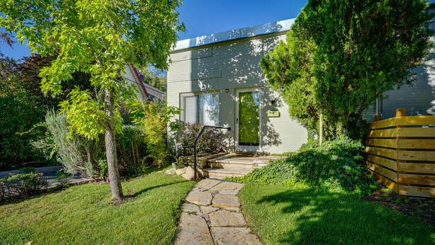Une maison avec un chemin de pierre menant à une porte verte, entourée d’une végétation luxuriante et d’une clôture en bois.