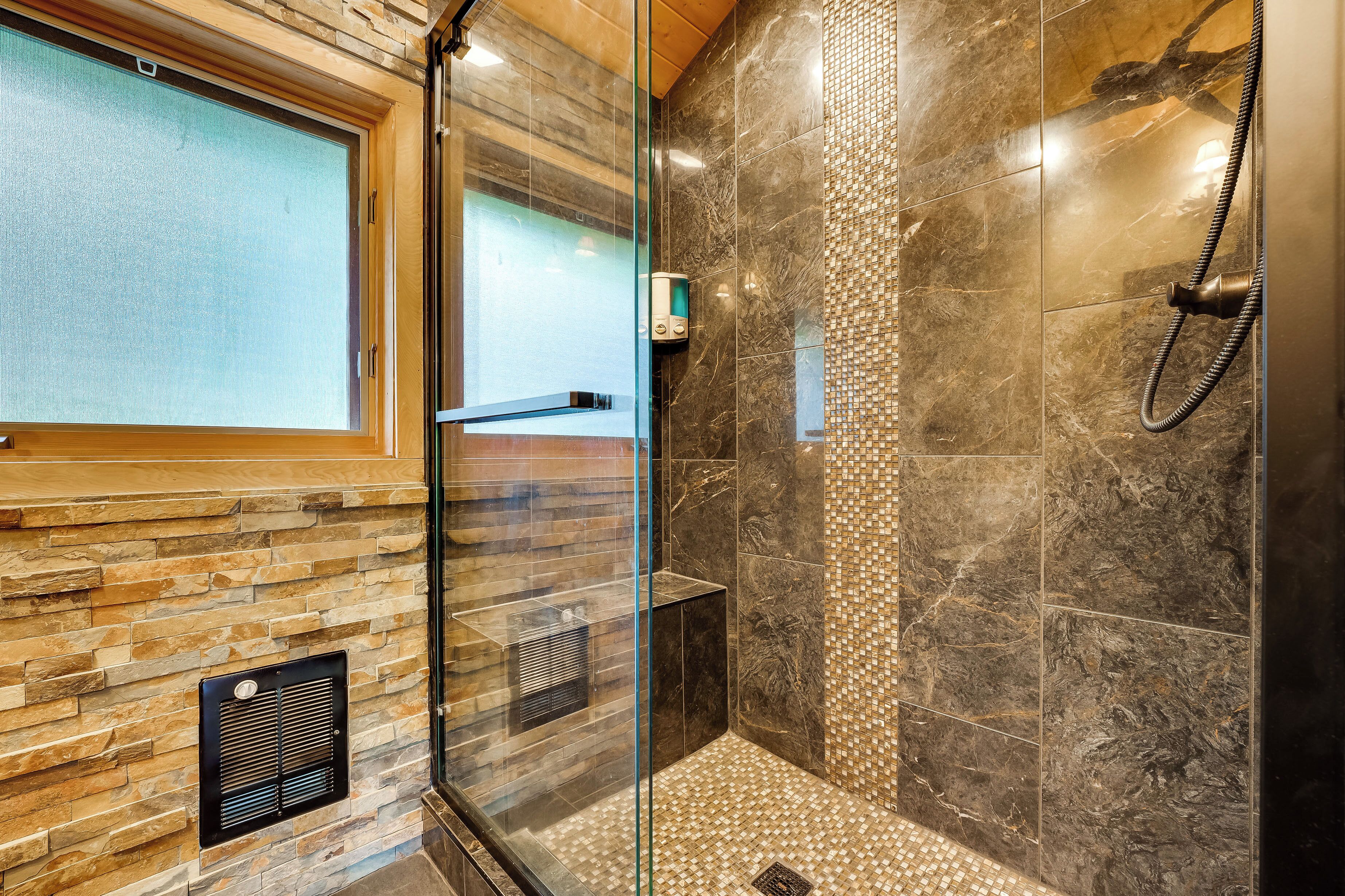 Un baño moderno con cabina de ducha de vidrio, paredes de piedra y azulejos, y un sistema de ventilación integrado.