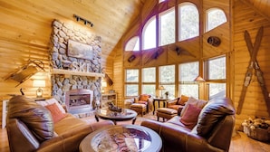 A cozy log cabin interior with leather sofas, a stone fireplace, and large windows. - Spacious Packwood Cabin w/ Hot Tub - Near River (Packwood)