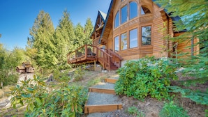 A wooden cabin with a deck, surrounded by dense forest and a stone pathway. - Spacious Packwood Cabin w/ Hot Tub - Near River (Packwood)