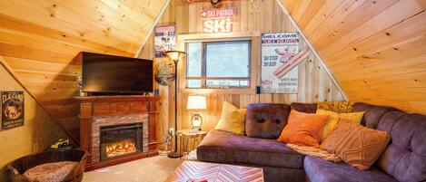 A cozy cabin interior with a fireplace, a couch, a television, and a sign indicating a ski patrol area.