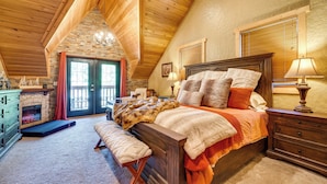 A cozy bedroom with a wooden ceiling, a stone fireplace, a bed with multiple pillows, and a bench. - Spacious Packwood Cabin w/ Hot Tub - Near River (Packwood)