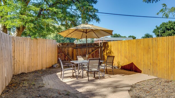 A patio with a table and chairs, a wooden fence, and a tree providing shade. - 9 Mi to Dtwn Denver: Aurora Vacation Rental (Aurora)