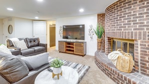 A living room with a brick fireplace, a leather sofa, a flat-screen TV, and a coffee table with a plant. - 9 Mi to Dtwn Denver: Aurora Vacation Rental (Aurora)