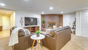 A living room with a brick fireplace, leather sofa, a TV, and a small table with a plant. - 9 Mi to Dtwn Denver: Aurora Vacation Rental (Aurora)