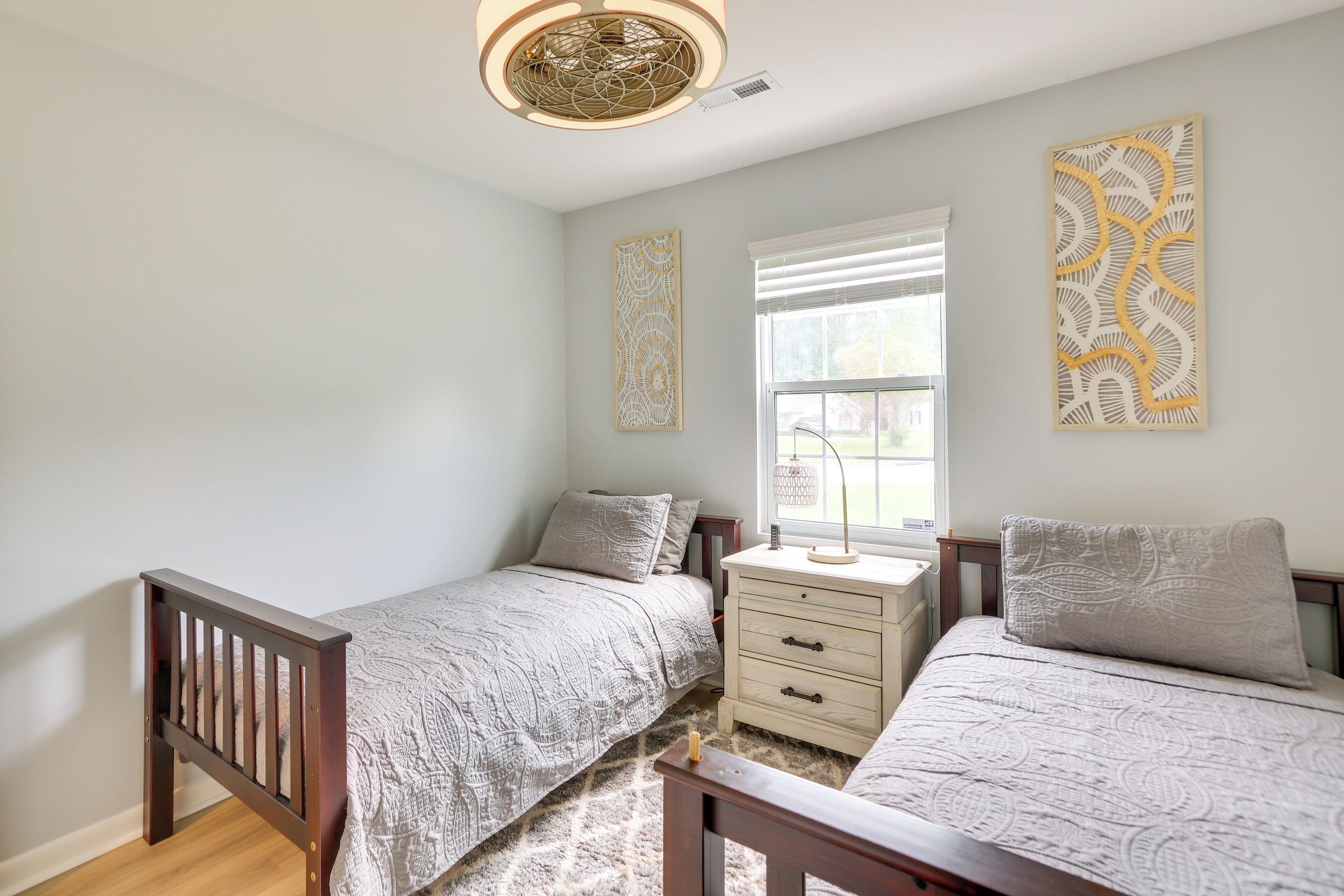 A bedroom with two beds, a nightstand, a dresser, and decorative wall art.