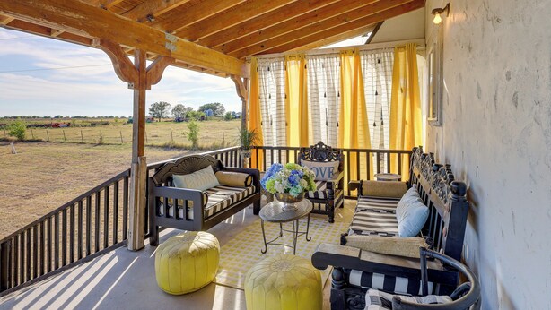 Een overdekt terras met houten meubels, een tafel met bloemen en uitzicht op het platteland.