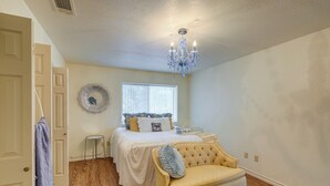 Een slaapkamer met een bed, een gele fauteuil, een kroonluchter en een raam.