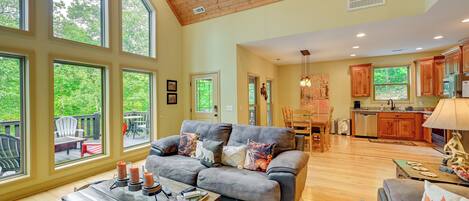 A spacious living area with a gray sofa, a wooden coffee table, and a view of the outdoors through large windows.